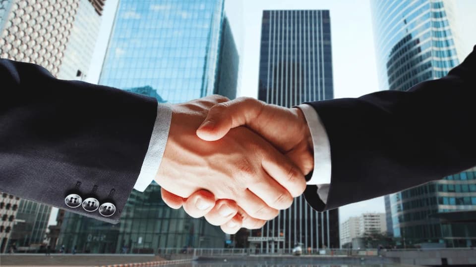 A professional handshake in front of city skyscrapers, representing Aayulogic's engineering partnership and trust